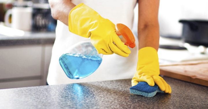 Person disinfecting kitchen counter top with cleaning solution