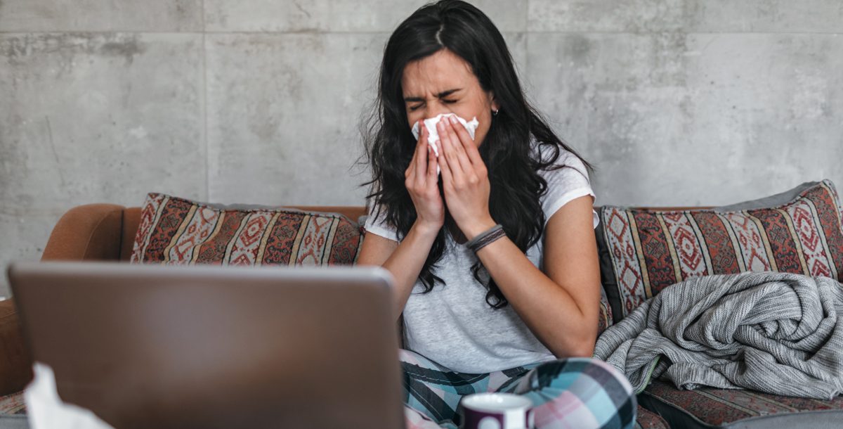 Woman blowing her nose while looking at computer screen.