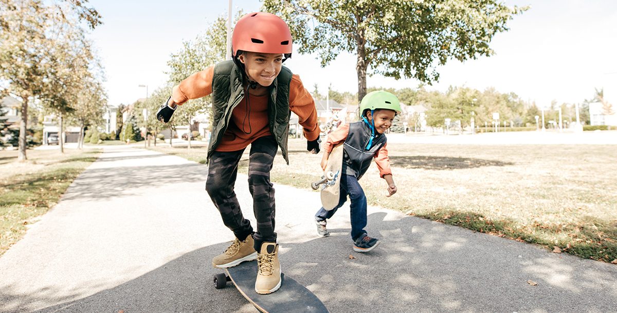 Two kids wearing helmets while skateboarding outside.