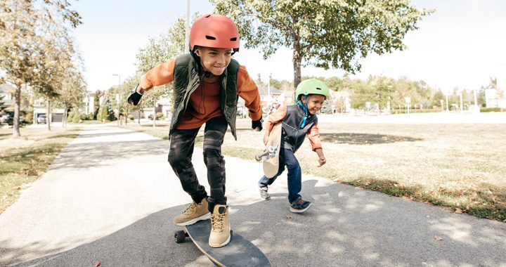 Two kids wearing helmets while skateboarding outside.