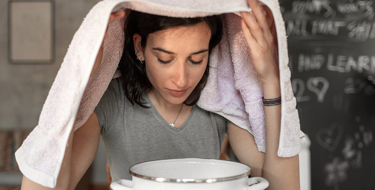 A woman clearing her nose and throat with steam from hot water.