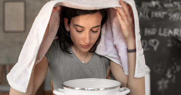 A woman clearing her nose and throat with steam from hot water.