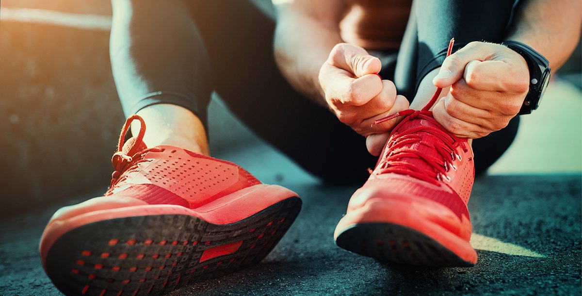 A runner lacing up their running shoes with orthotic inserts.