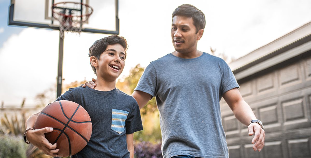 A father playing basketball with his son outside during COVID-19.