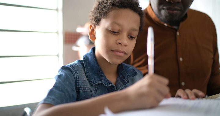 A young boy working on school work at home with a parent.