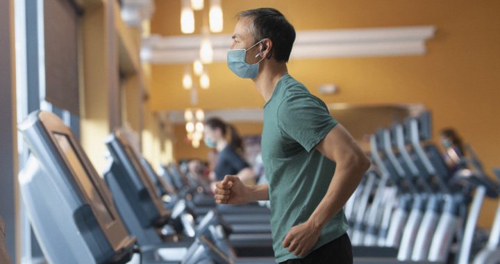 A man working out at the gym while wearing a face mask.