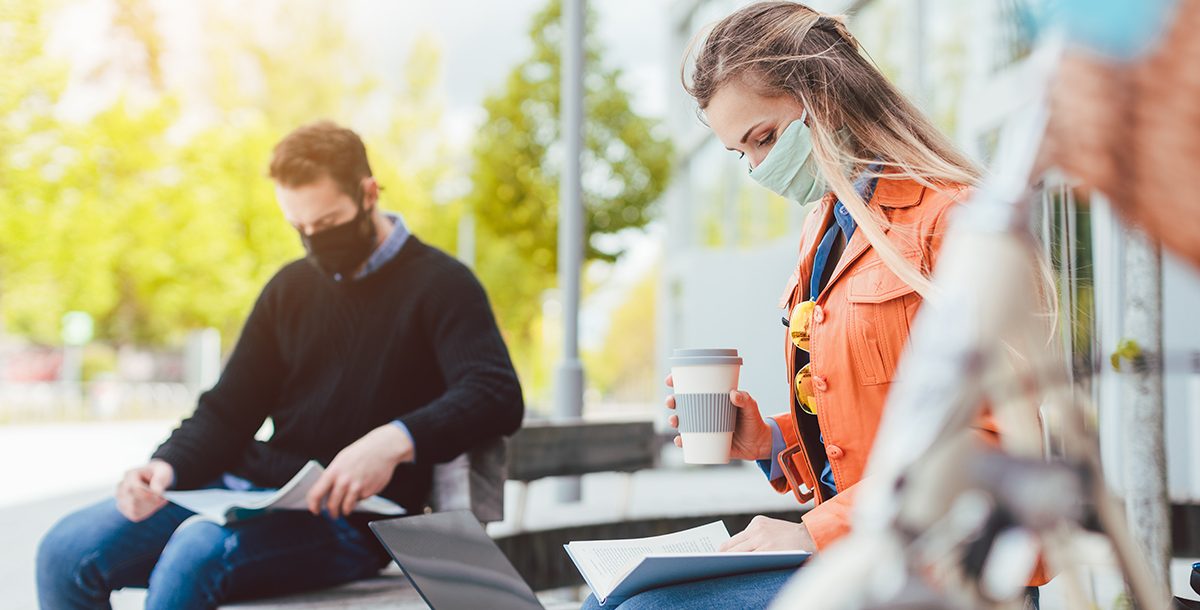 A woman and man wearing face masks while sitting outdoors.