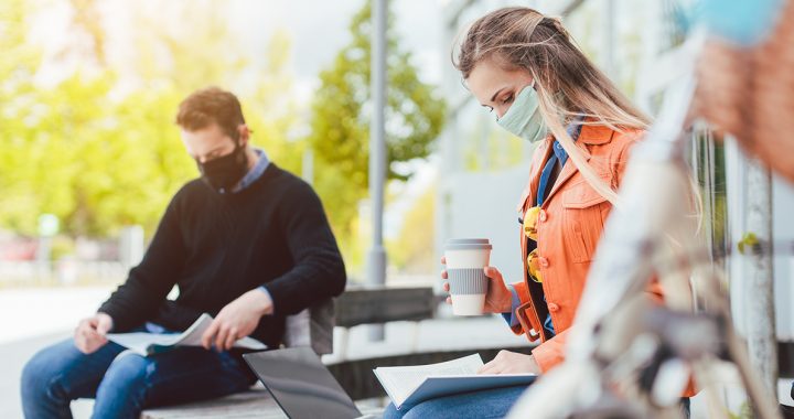 A woman and man wearing face masks while sitting outdoors.