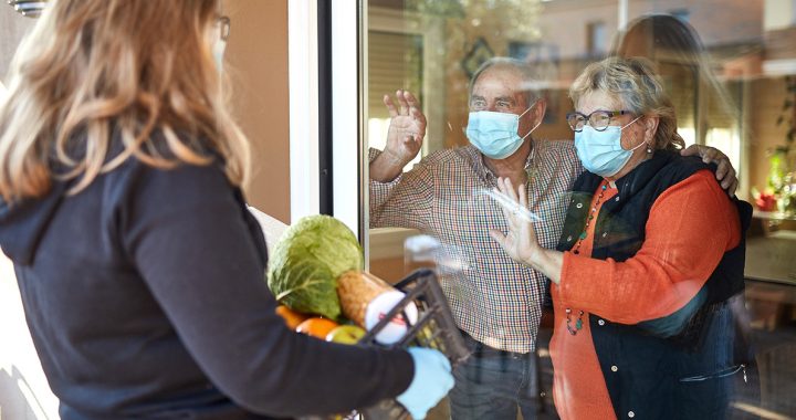 A volunteer delivering food to an older couple.