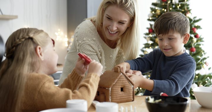 A mom decorating a gingerbread house with her kids.